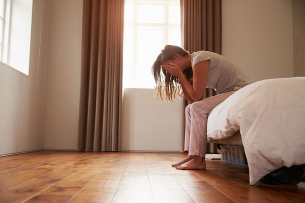 Woman sitting on edge of bed with her head in her hands