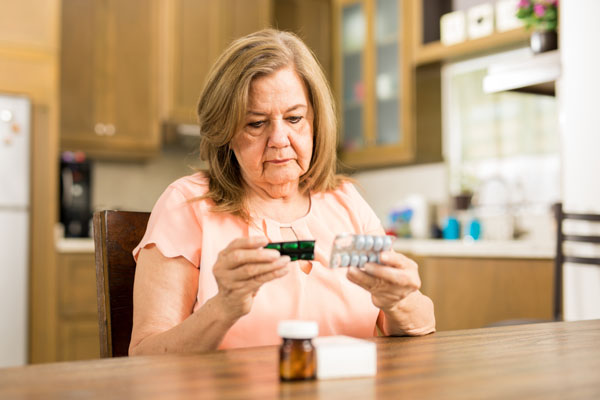 Elderly woman sitting at the table reading her medicine label