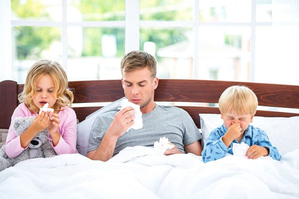 Father with two children sick in bed blowing their noses