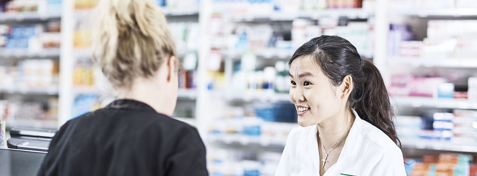 Smiling Pharmacist speaking with a customer at the shop counter